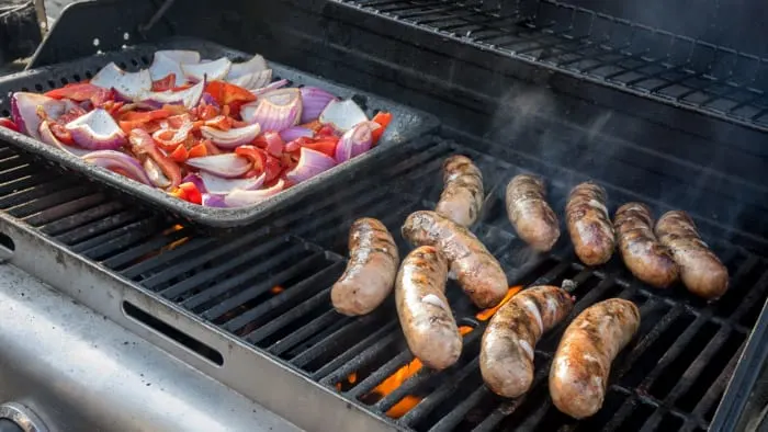 Ernesto grills Italian sausages and peppers and onions to contribute to the community potluck. 