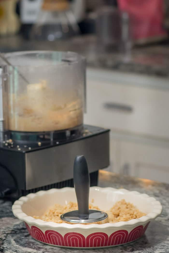 Using a meat pounder to press the shortbread crumbs into a pie crust.