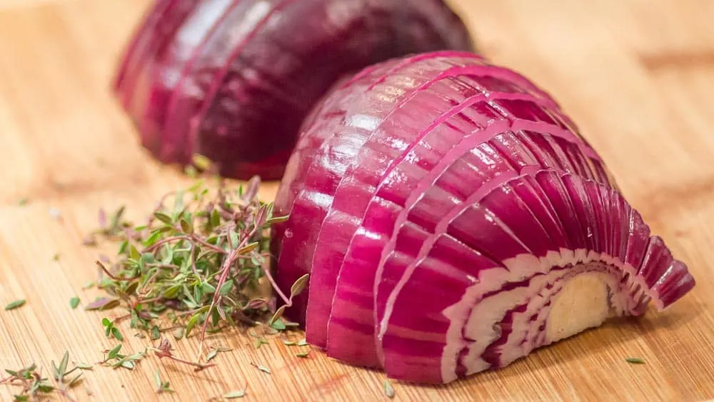 The cutting board has sliced red onions and sprigs of thyme, ready to be sautéd.