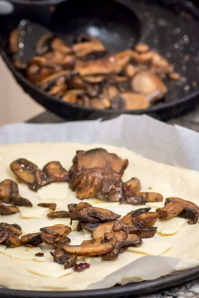 Applying the sautéd mushrooms to the unbaked crust.