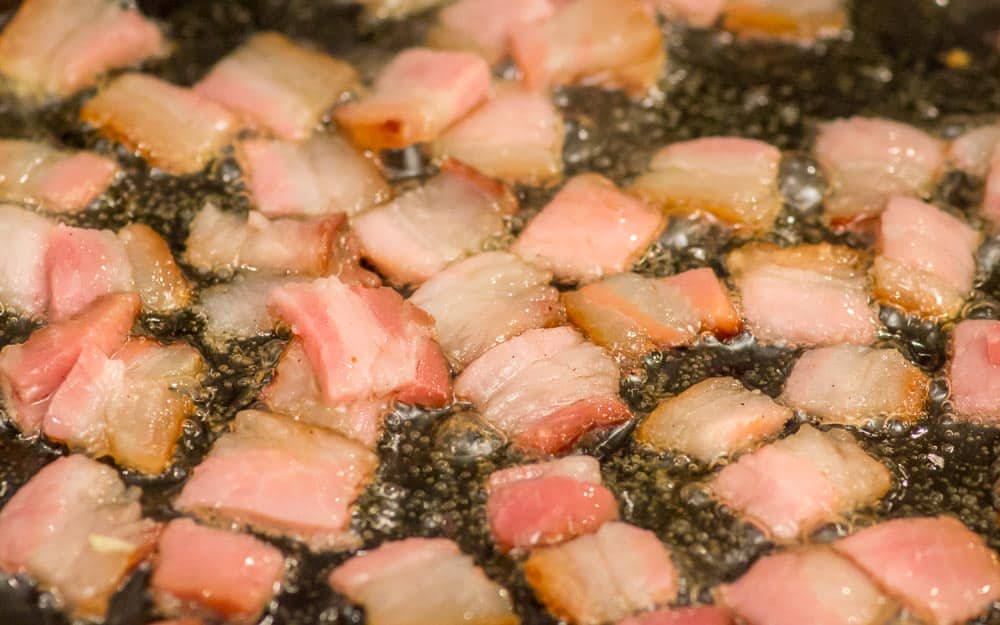 Frying up the little pieces of bacon.