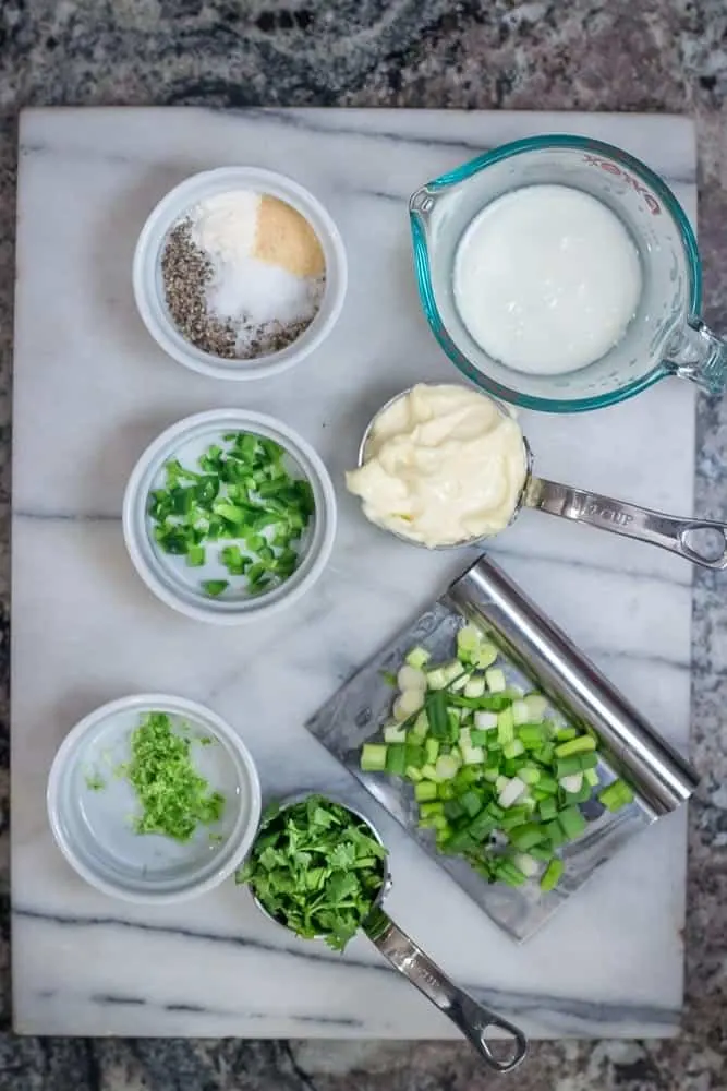 A picture of all the ingredients for the dressing: buttermilk, mayonnaise, chopped scallions, chopped cilantro, lime zest, onion powder, garlic powder and salt & pepper.