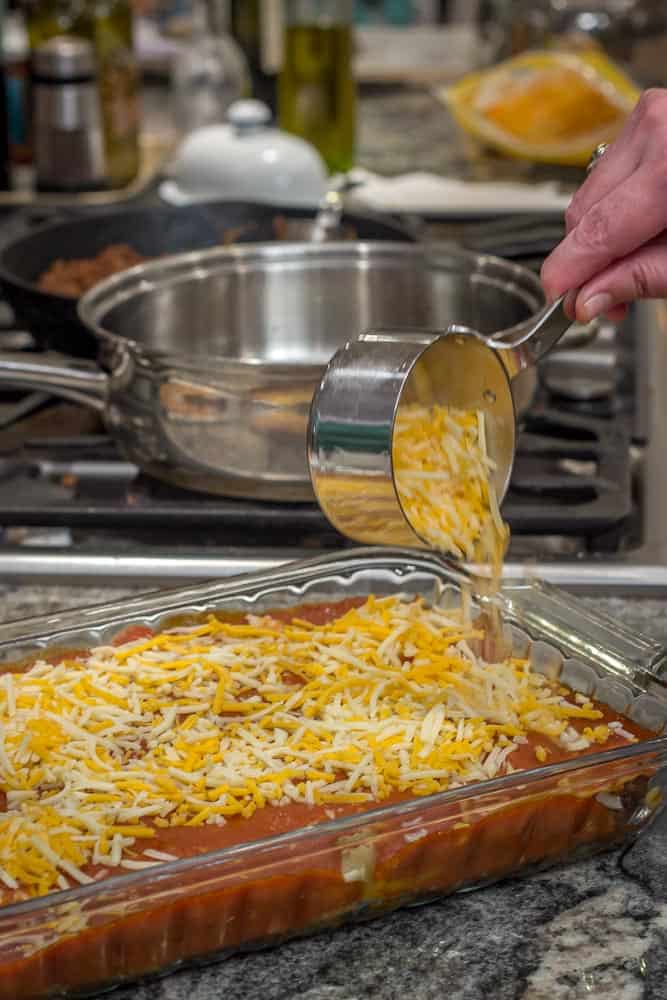 Topping the pan of enchiladas with a blend of cheeses.