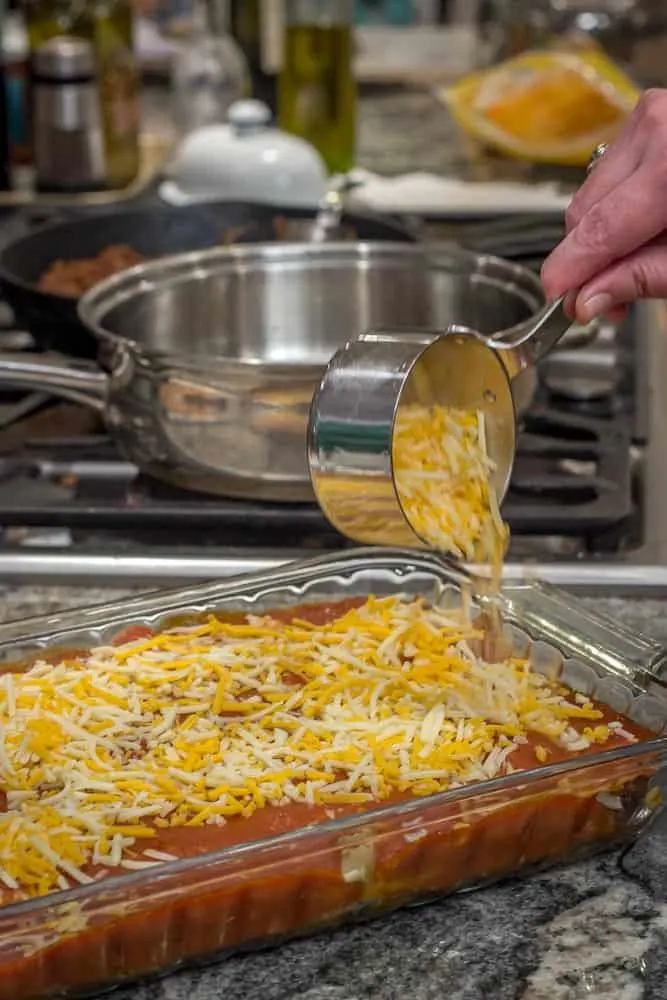 Topping the pan of enchiladas with a blend of cheeses.