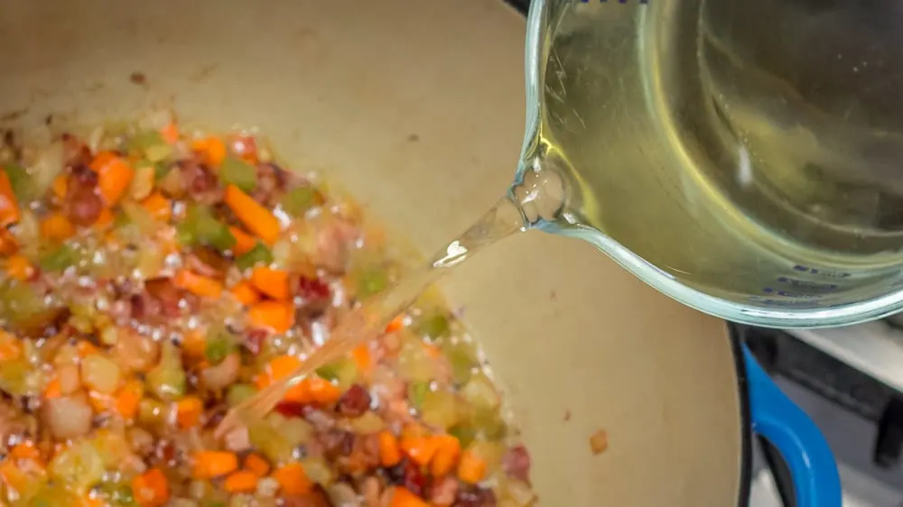 Adding wine to the bacon and veggies.