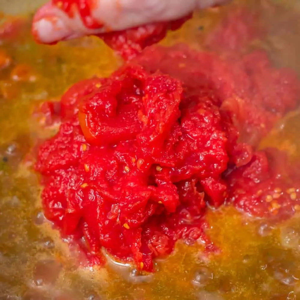 Squishing the tomatoes with my hands into the simmering stew.