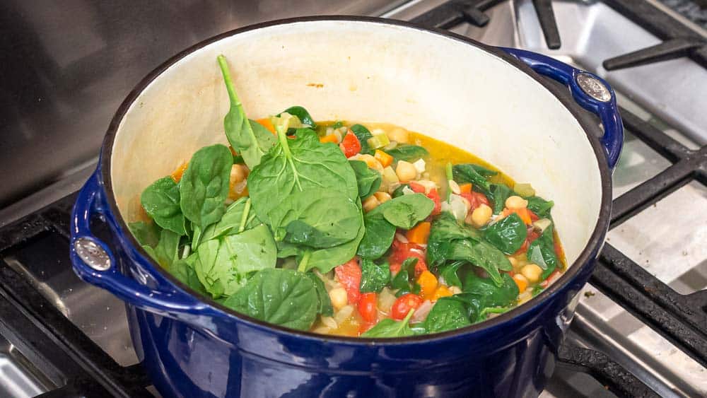 Adding the raw spinach to the pot, to just wilt it.