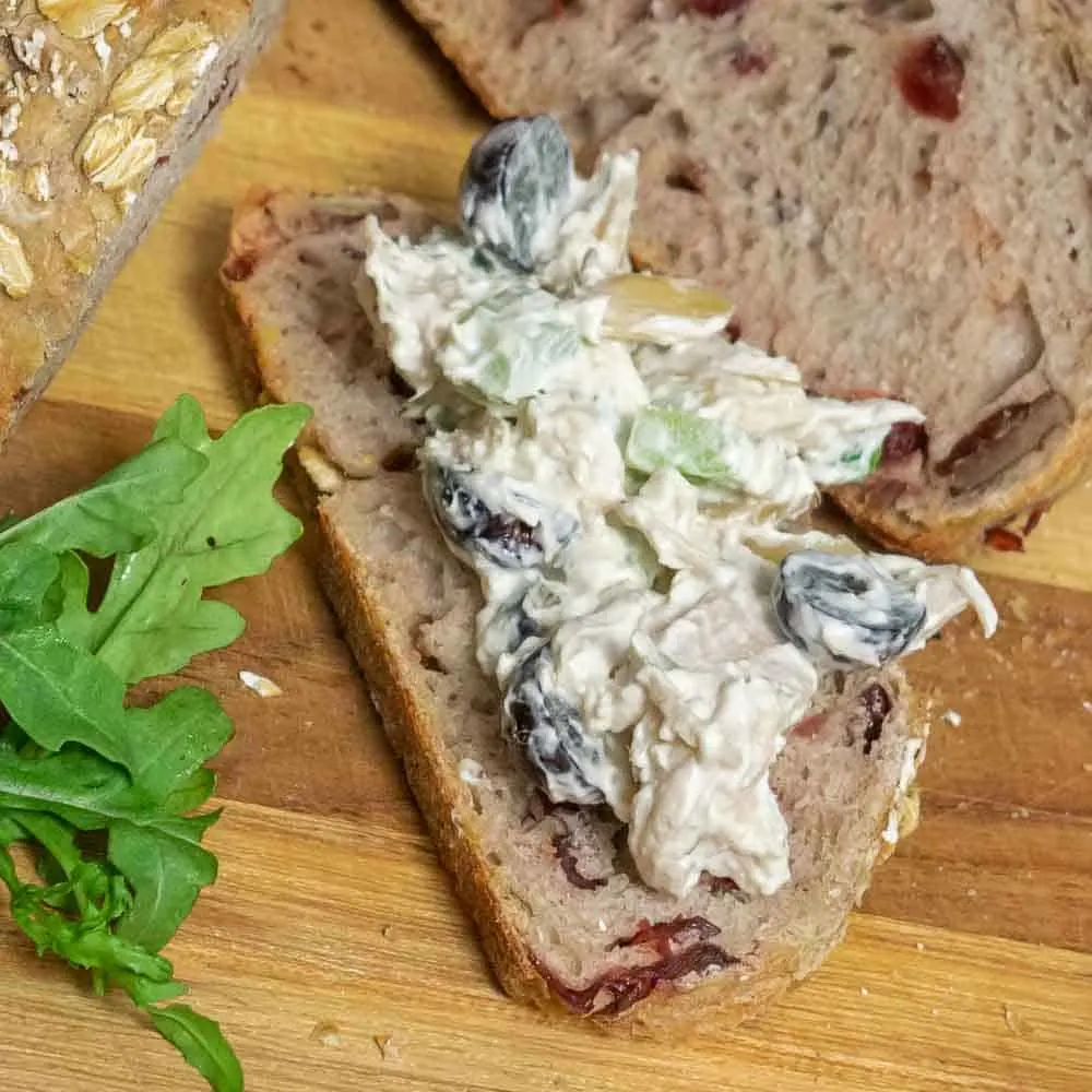 Closeup of chicken salad on cranberry pecan sourdough loaf with arugula.