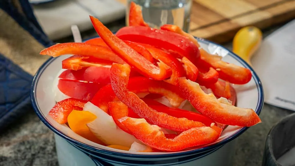 Bowl full of sliced peppers and onions.