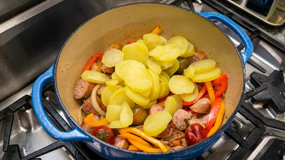 Adding the sliced cooked potatoes to the pot.