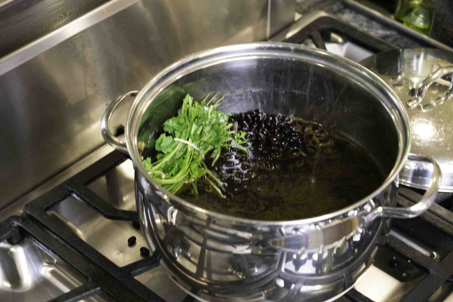 a pot of black beans being cooked with a cilantro bundle
