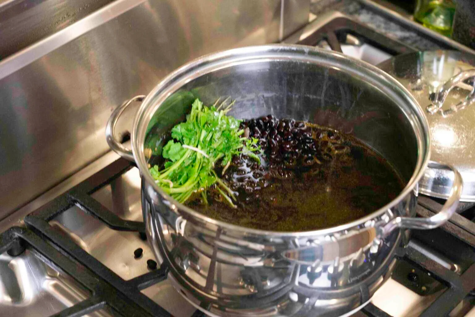 a pot of black beans being cooked with a cilantro bundle